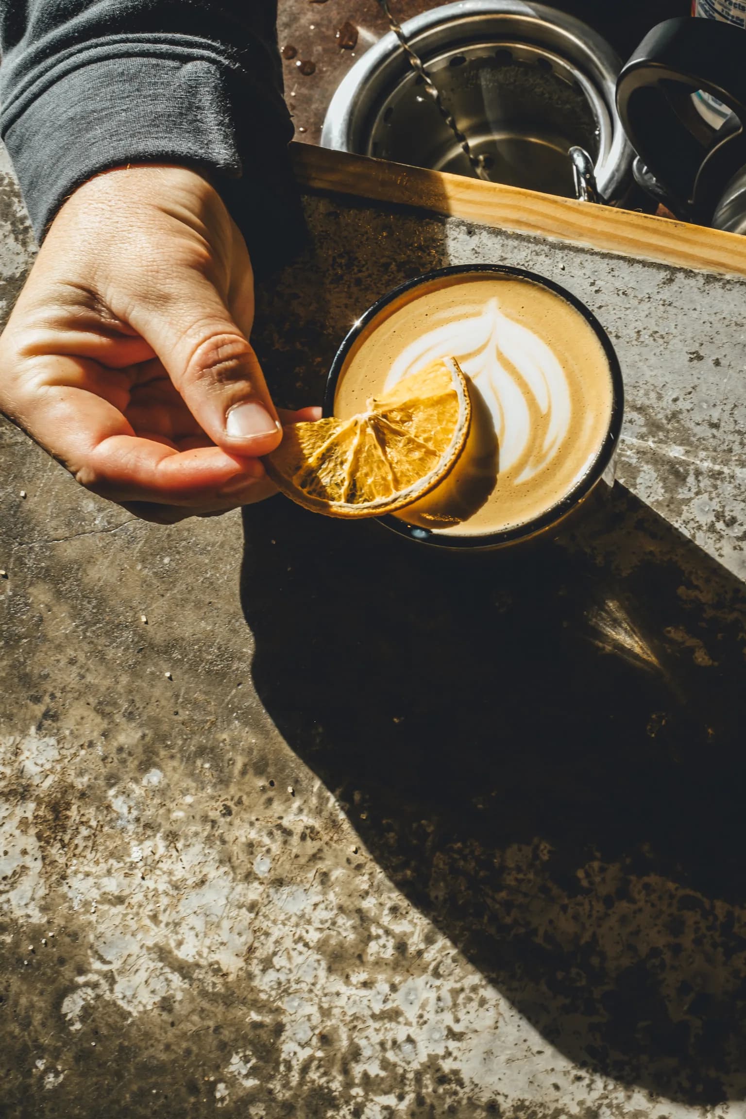 Hands finishing a crafted Corner Coffee drink with a dried citrus garnish